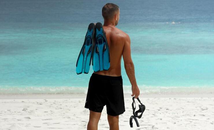 person standing on beach holding snorkel, mask and fins