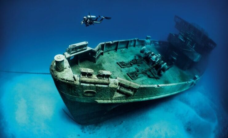 picture of person scuba diving with kittiwake shipwreck in the background